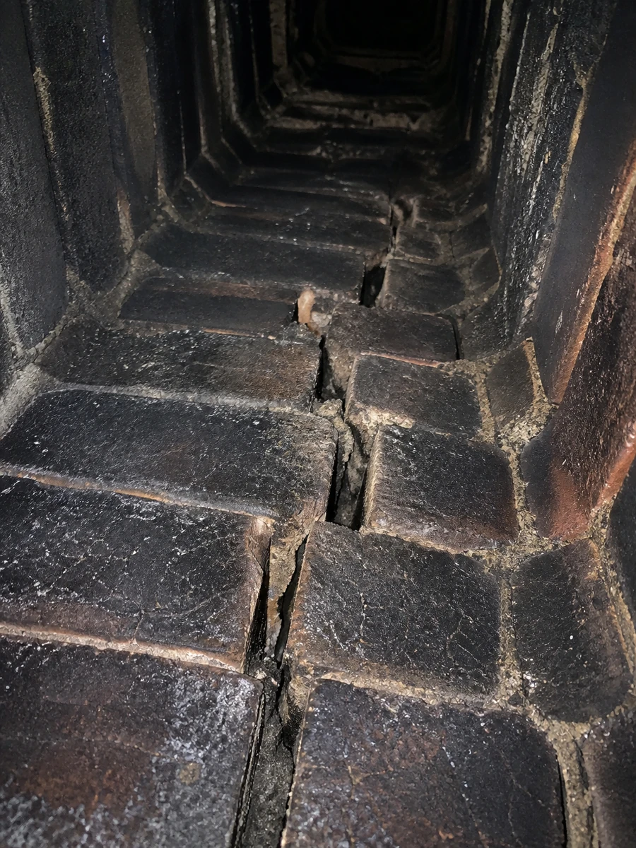 Intérieur d'un conduit de cheminée en briques, noirci par la suie et fissuré, signe d'un défaut d'entretien ou de conception