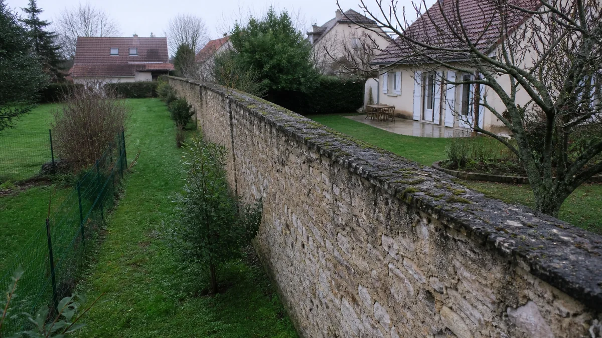Mur mitoyen en pierre séparant deux jardins de pavillons franciliens, borne cadastrale visible au pied du mur