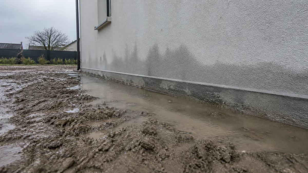 Flaque d'eau stagnante contre le pied d'un mur de fondation après une pluie, signe d'un drainage défaillant