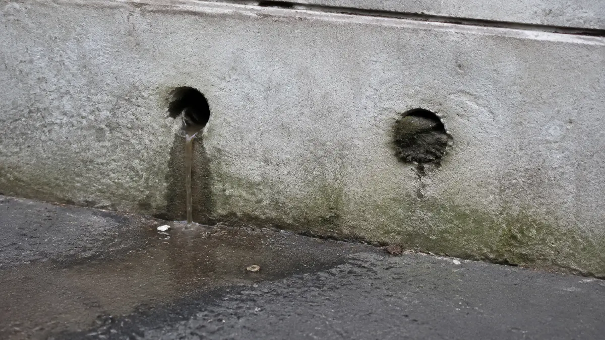 Deux barbacanes en pied de mur de soutènement, l'une laissant écouler un filet d'eau, l'autre obstruée et sèche