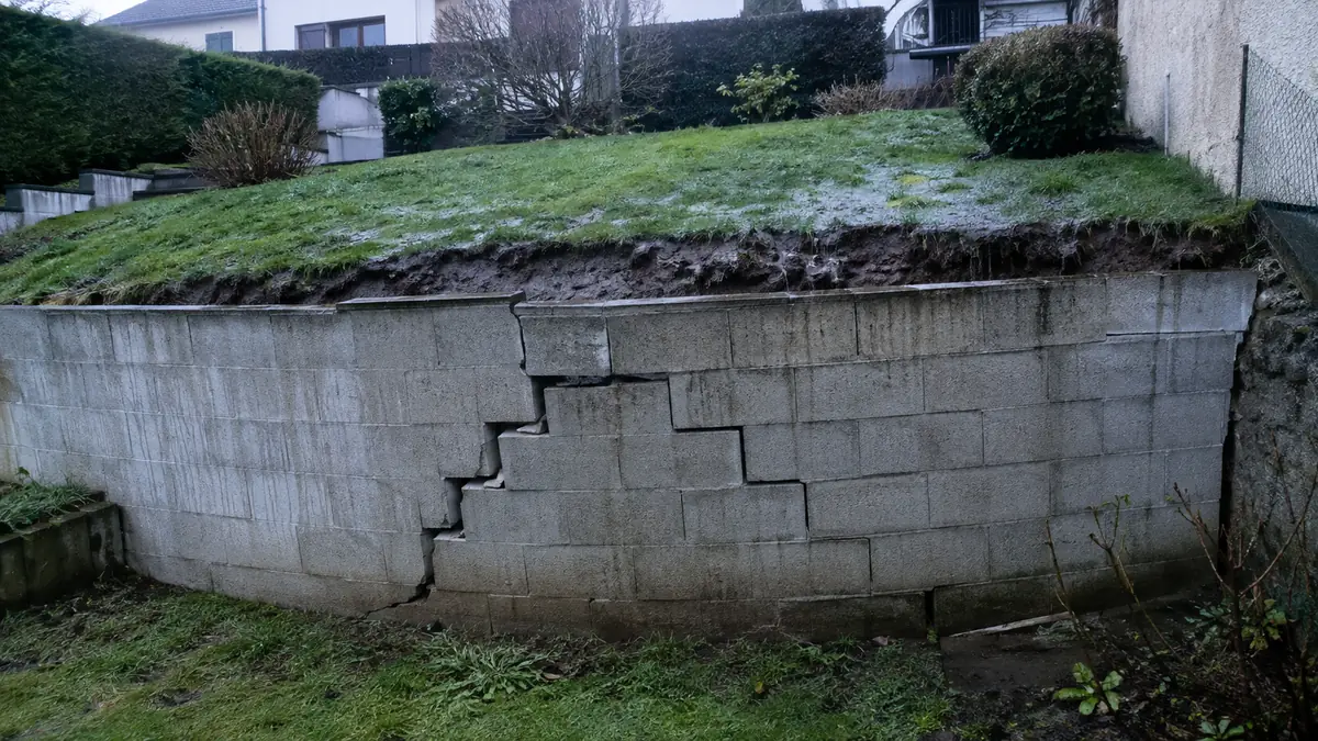 Mur de soutènement en parpaings penché vers l’avant, ventre marqué et fissure en escalier dans la maçonnerie