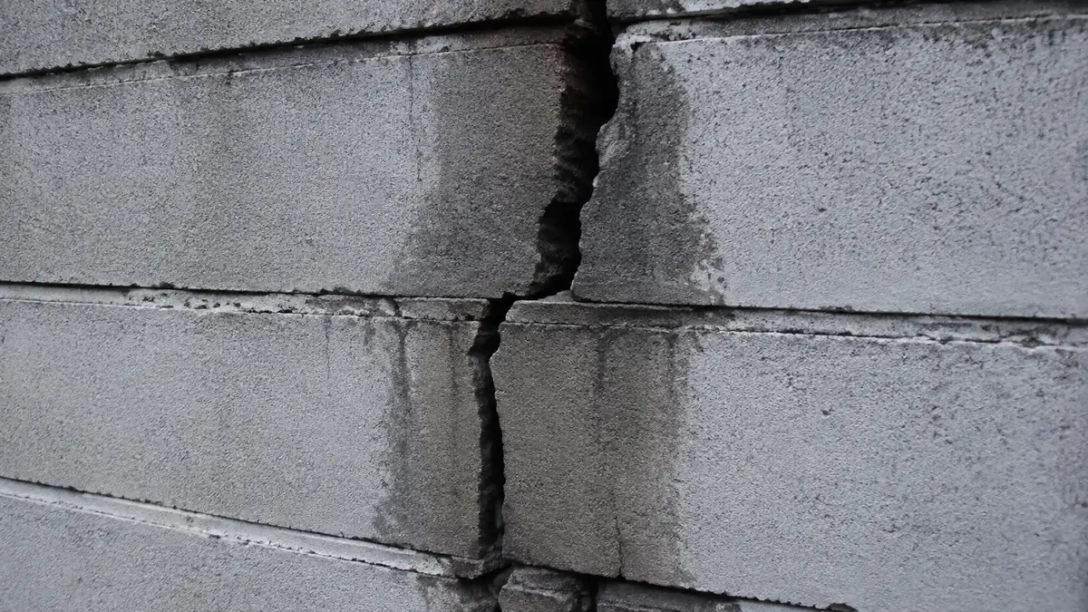 Fissure verticale large traversant un mur de soutènement, avec traces d'humidité sur les bords