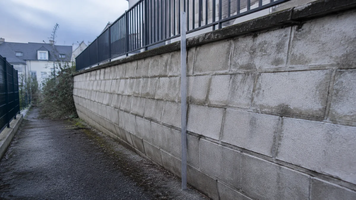 Vue oblique d'un mur de soutènement présentant un ventre marqué, un fil à plomb tendu révélant le hors d'aplomb