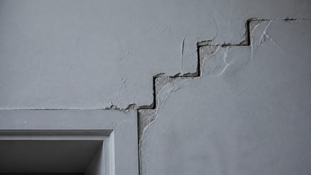 Fissure en escalier partant de l'angle supérieur d'une ouverture et remontant dans l'enduit d'un mur en blocs