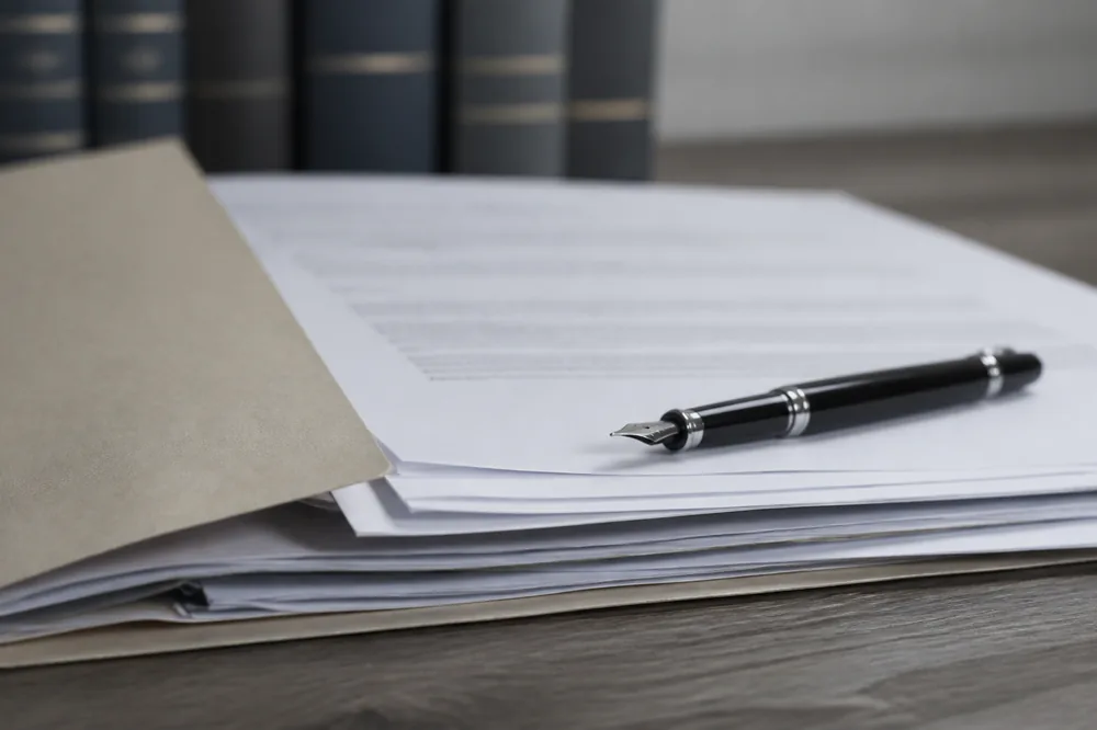 Dossier de procédure avec courriers, pièces annotées et stylo, posé sur un bureau, piles de codes juridiques floues en arrière-plan