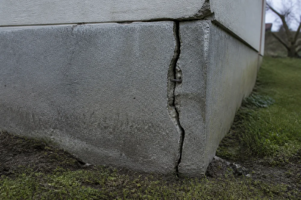 Fissure verticale dans un soubassement de fondation, avec léger affaissement du sol en pied de mur