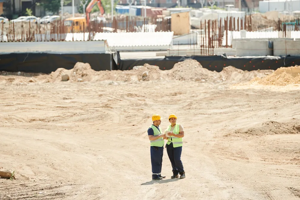 Deux professionnels du bâtiment échangeant sur un chantier de construction, plans à l'appui